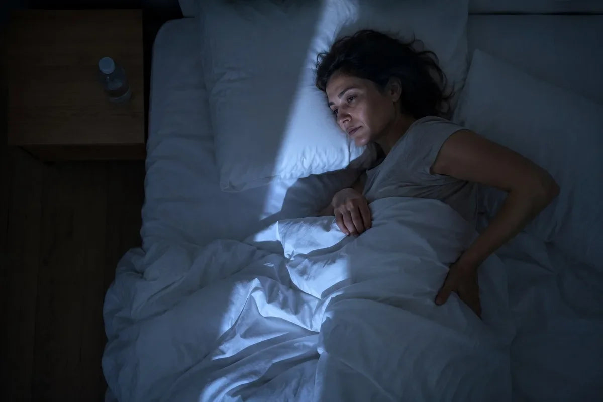 Person liegt nachts wach im Bett, Hand am unteren Rücken — der Moment der schlaflosen Nacht